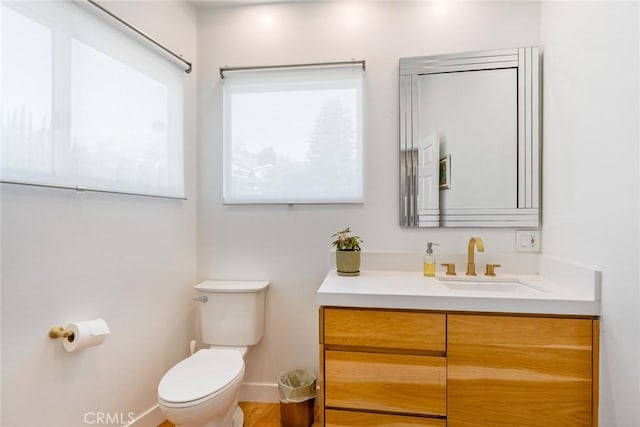 half bath with baseboards, toilet, and vanity