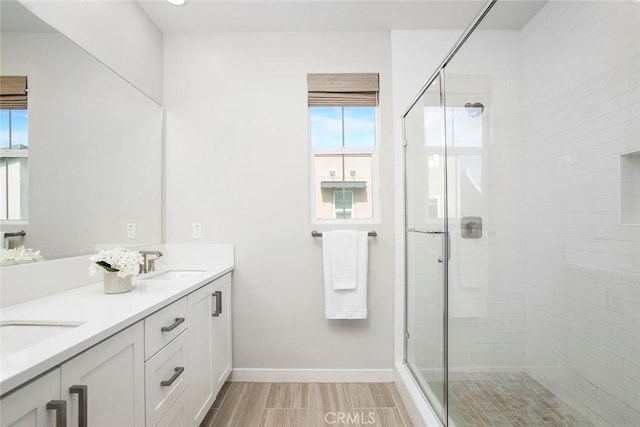 full bathroom with wood finish floors, a stall shower, a sink, and baseboards