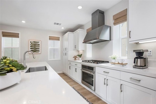 kitchen with wall chimney range hood, appliances with stainless steel finishes, light countertops, and a sink