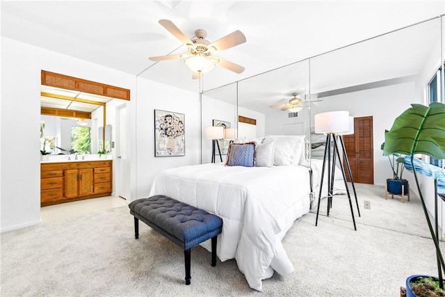 bedroom featuring light colored carpet, ensuite bath, and ceiling fan