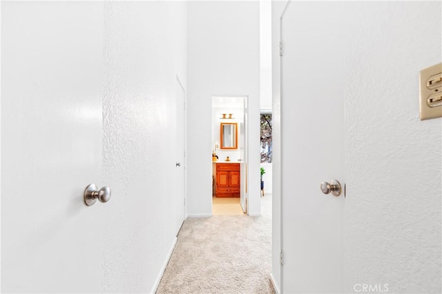 hall featuring light colored carpet, baseboards, and a textured wall