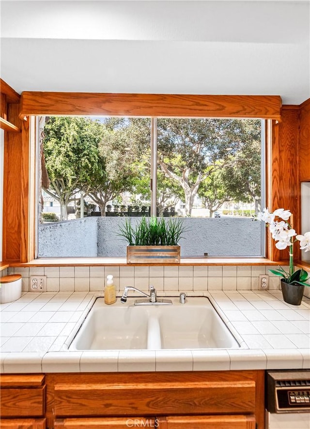 kitchen with brown cabinetry, tile countertops, and a sink