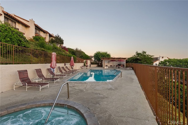 pool at dusk featuring a patio area and a community hot tub