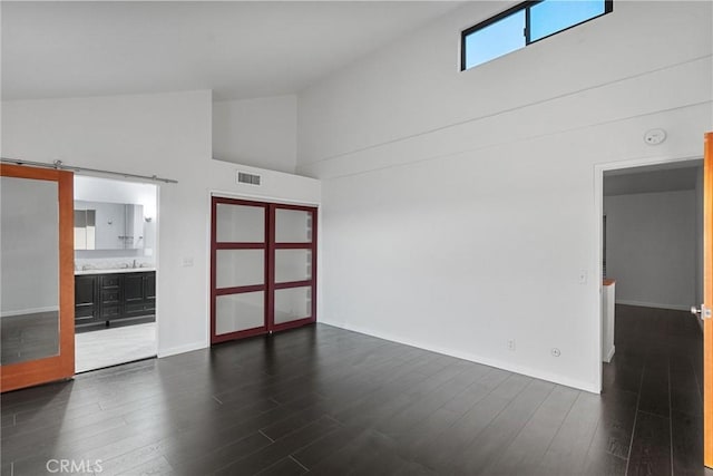 empty room with high vaulted ceiling, dark hardwood / wood-style flooring, and a barn door