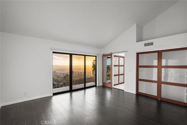 spare room with a barn door, high vaulted ceiling, and dark hardwood / wood-style floors