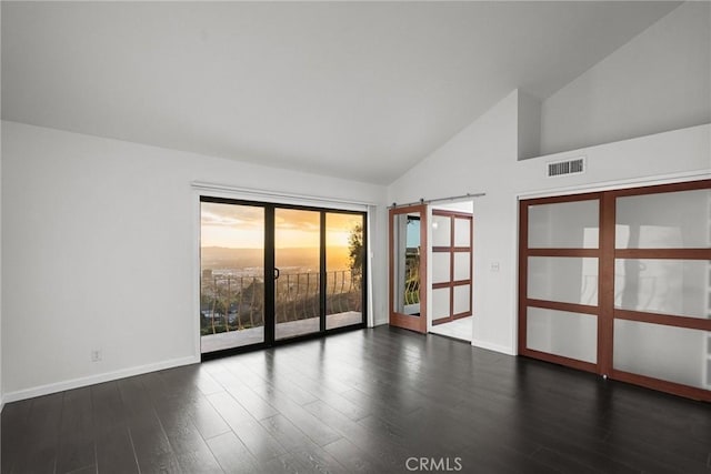 empty room with dark hardwood / wood-style flooring, a barn door, and high vaulted ceiling