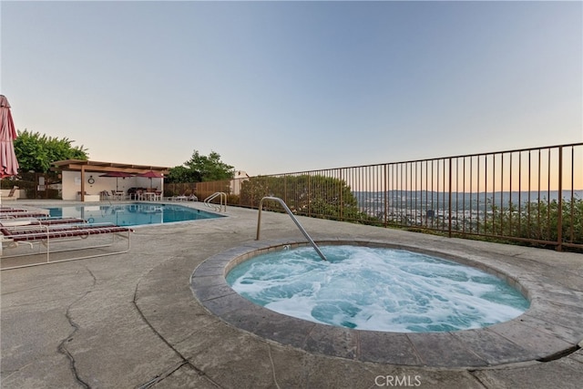 pool at dusk with a patio area and a community hot tub