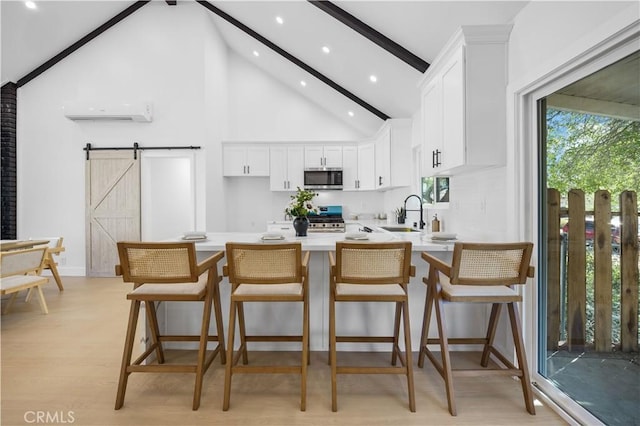 kitchen featuring a barn door, a wall unit AC, appliances with stainless steel finishes, white cabinets, and a breakfast bar area