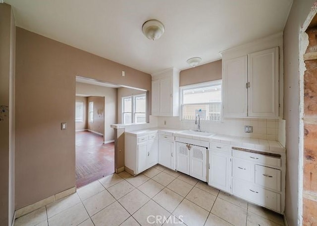 kitchen with white cabinets, tile countertops, a sink, backsplash, and light tile patterned floors