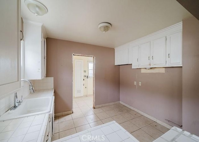 laundry room with baseboards, a sink, and light tile patterned floors