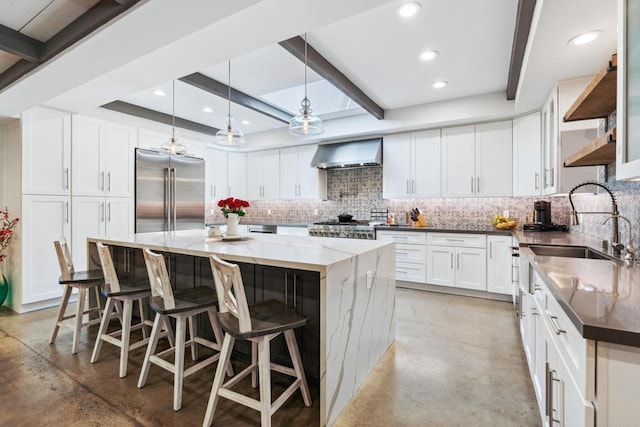 kitchen with white cabinetry, stainless steel built in refrigerator, wall chimney exhaust hood, and a kitchen island