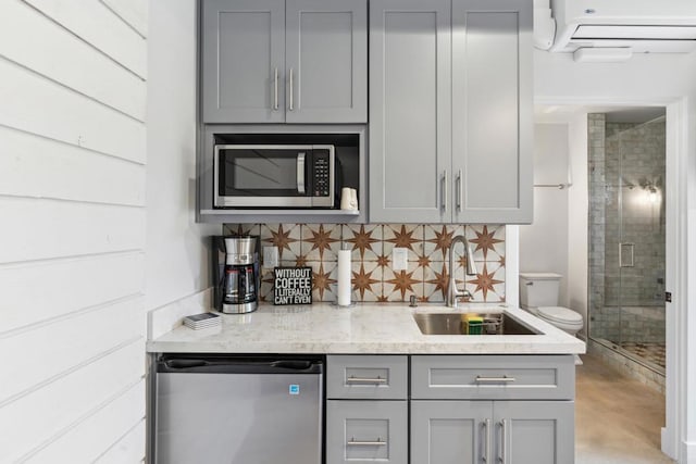 interior space featuring appliances with stainless steel finishes, gray cabinetry, decorative backsplash, sink, and a wall unit AC