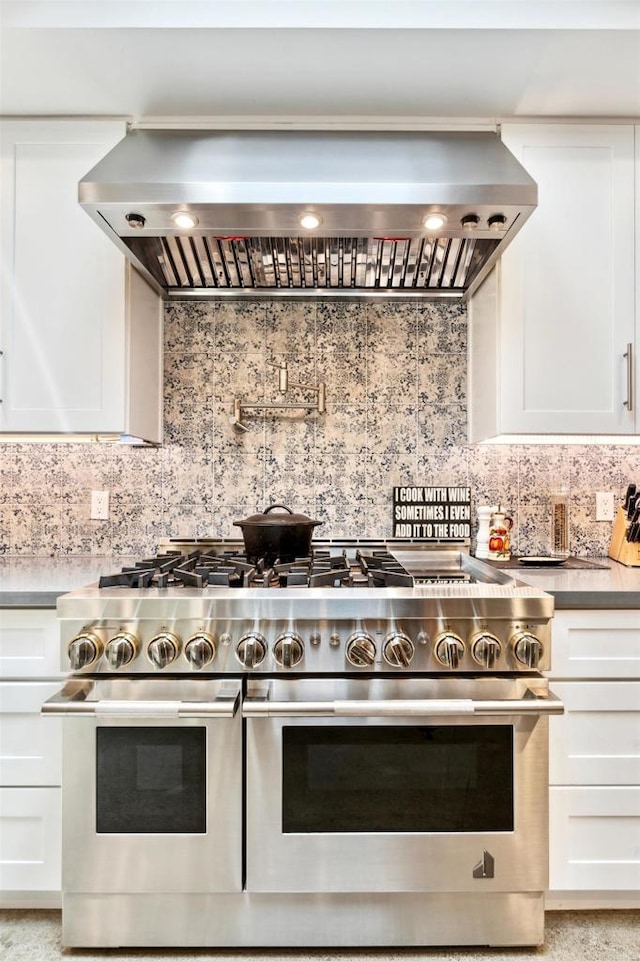 kitchen with decorative backsplash, wall chimney exhaust hood, range with two ovens, and white cabinets