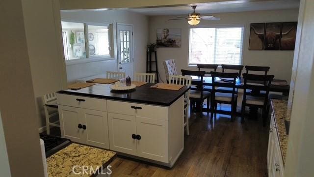 kitchen featuring dark wood-style floors, a center island, dark countertops, a ceiling fan, and white cabinetry