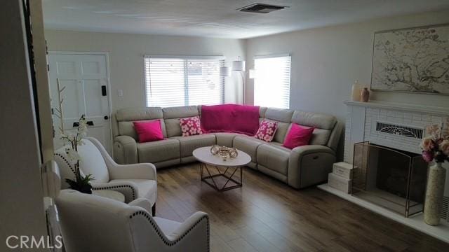 living area featuring a brick fireplace, visible vents, and wood finished floors