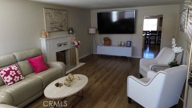 living area featuring a fireplace, baseboards, and dark wood-type flooring