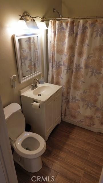 bathroom featuring toilet, a shower with shower curtain, wood finished floors, and vanity