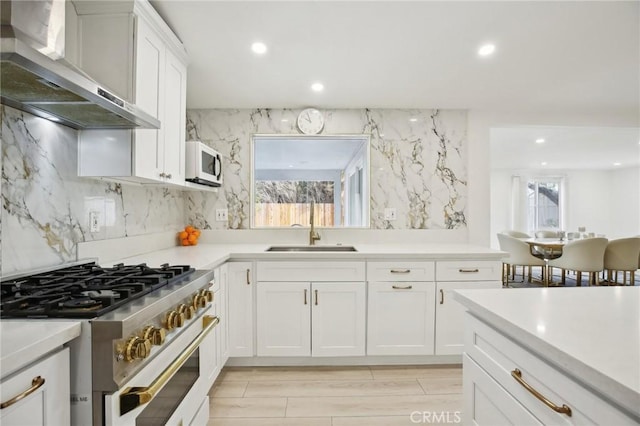 kitchen with sink, stainless steel range, tasteful backsplash, white cabinets, and wall chimney range hood