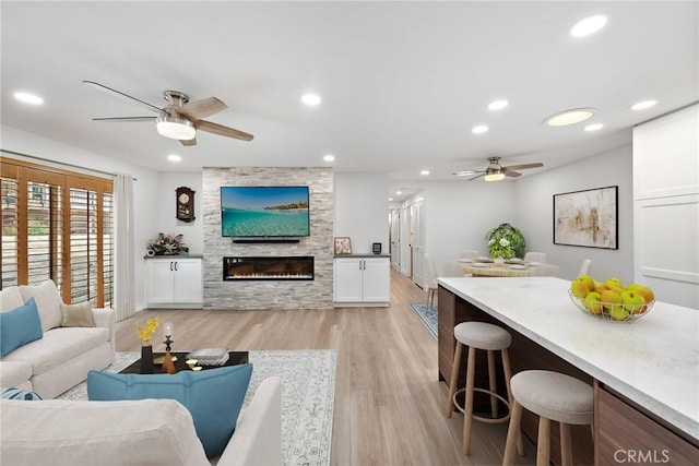 living room featuring light hardwood / wood-style flooring, ceiling fan, and a stone fireplace