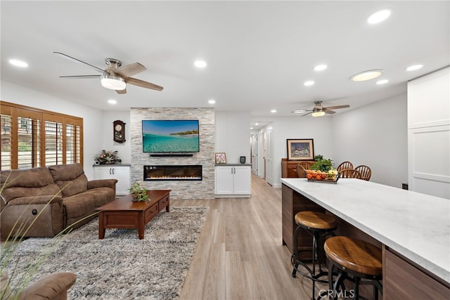 living room with a fireplace, ceiling fan, and light hardwood / wood-style floors