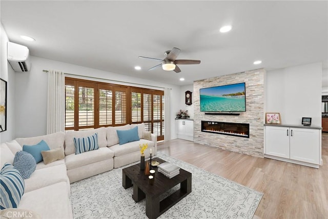 living room with an AC wall unit, light hardwood / wood-style floors, ceiling fan, and a fireplace