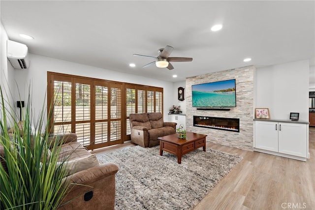 living room featuring a fireplace, ceiling fan, a wall mounted air conditioner, and light hardwood / wood-style floors