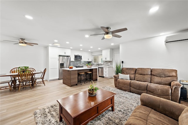 living room with an AC wall unit, ceiling fan, sink, and light hardwood / wood-style floors