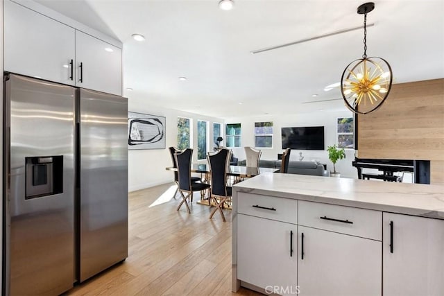 kitchen featuring white cabinets, hanging light fixtures, stainless steel fridge, and light stone counters