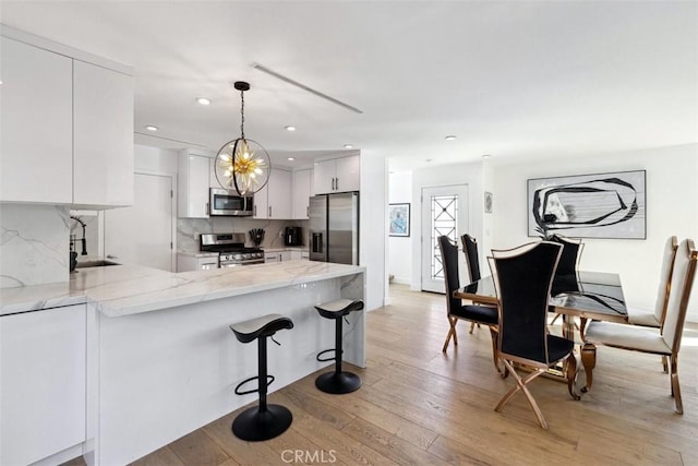 kitchen with sink, stainless steel appliances, kitchen peninsula, white cabinets, and hanging light fixtures