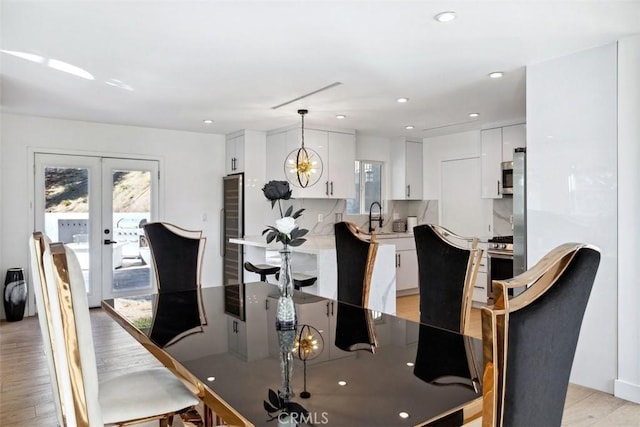 dining area featuring light hardwood / wood-style floors, french doors, sink, and a chandelier