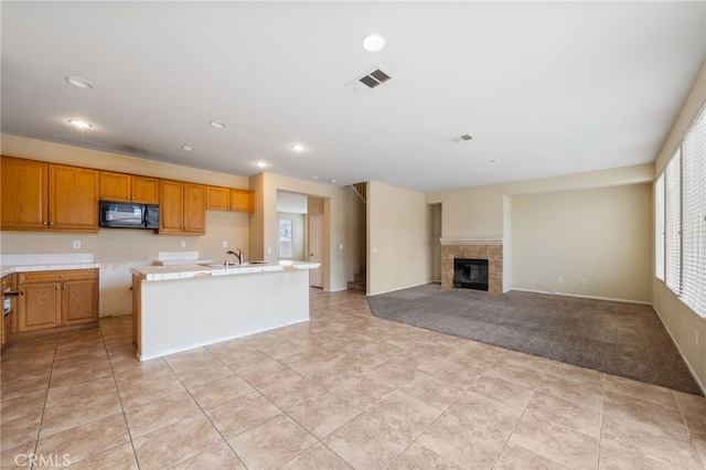 kitchen featuring a center island with sink, a tiled fireplace, sink, and light tile patterned flooring