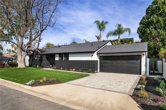 view of front of house with an attached garage, roof with shingles, decorative driveway, stucco siding, and a front lawn