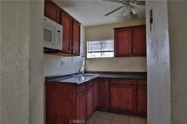 kitchen with a sink, a ceiling fan, light tile patterned floors, dark countertops, and white microwave