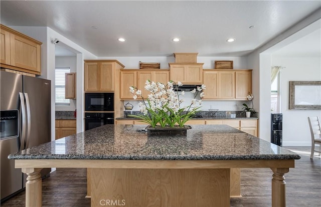 kitchen featuring a center island with sink, dark stone counters, light brown cabinetry, and black appliances