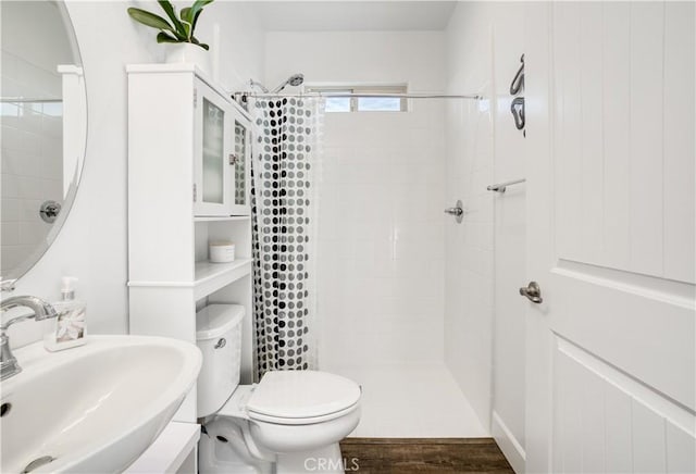 bathroom with hardwood / wood-style floors, tiled shower, sink, and toilet