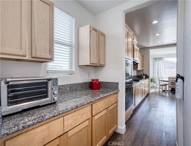 kitchen with dark stone counters, black oven, and light brown cabinetry