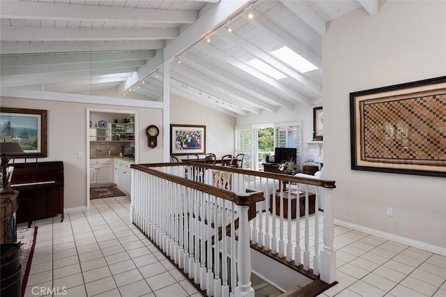 hall featuring vaulted ceiling with beams, baseboards, light tile patterned floors, and an upstairs landing