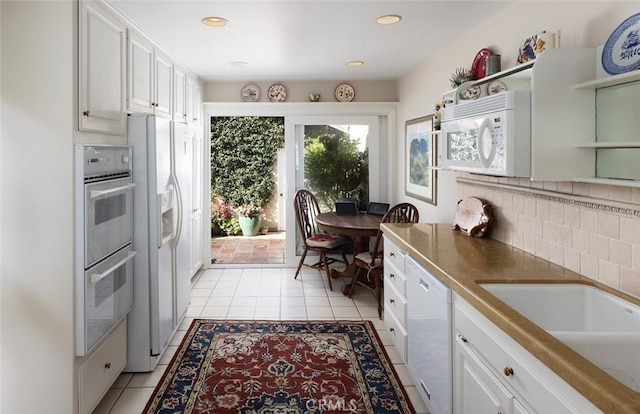 kitchen featuring light tile patterned floors, tasteful backsplash, white appliances, white cabinetry, and a sink