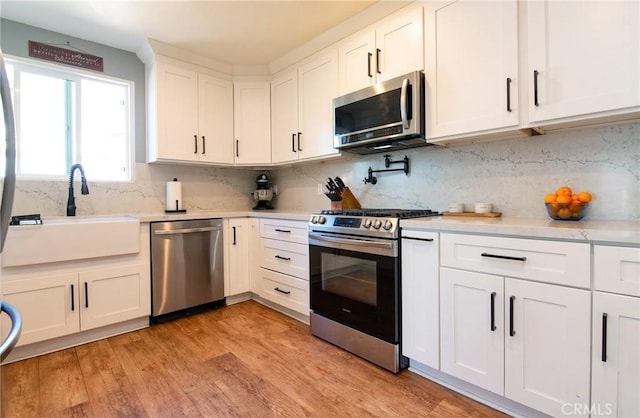 kitchen with a sink, white cabinetry, light wood-style floors, appliances with stainless steel finishes, and light countertops