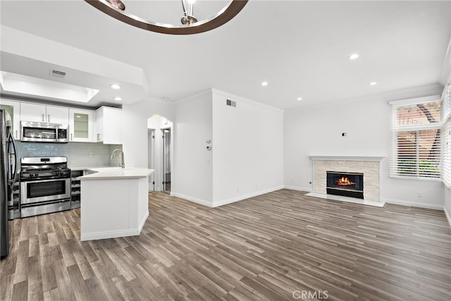 kitchen featuring hardwood / wood-style floors, appliances with stainless steel finishes, white cabinets, ornamental molding, and decorative backsplash