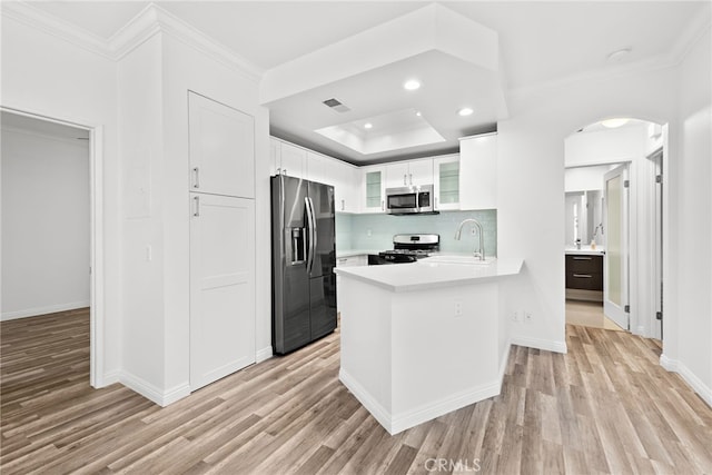 kitchen with sink, light wood-type flooring, stainless steel appliances, kitchen peninsula, and white cabinets