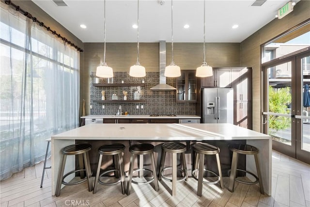 kitchen featuring a breakfast bar, stainless steel fridge, wall chimney exhaust hood, and pendant lighting