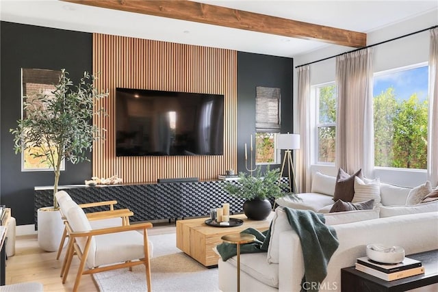 living room with an accent wall, beamed ceiling, and light wood-style floors