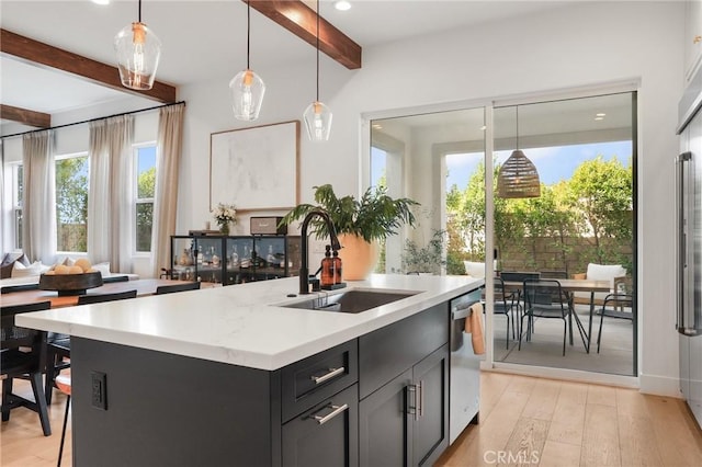 kitchen with hanging light fixtures, a sink, a kitchen island with sink, beam ceiling, and stainless steel dishwasher