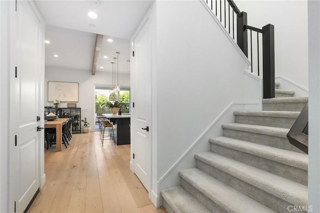 stairs featuring recessed lighting, beam ceiling, and wood finished floors