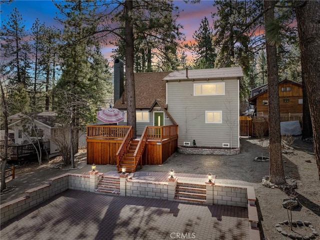 back of house at dusk featuring a patio, a chimney, stairway, fence, and a deck