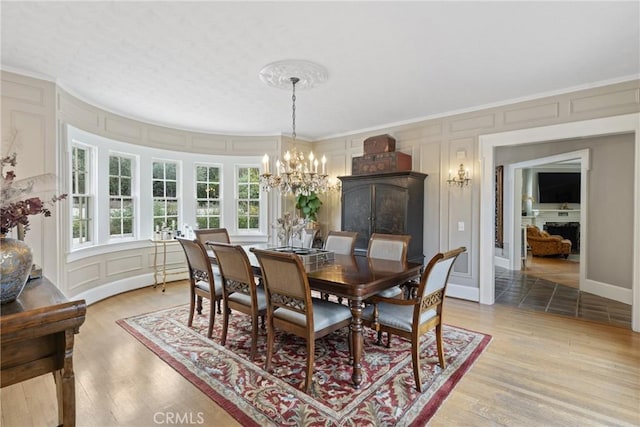 1205 W Highland Ave, Redlands, CA 92373 - dining space featuring a decorative wall, a chandelier, crown molding, and light wood-type flooring
