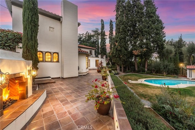 1205 W Highland Ave, Redlands, CA 92373 - pool at dusk featuring a tile fireplace, a patio area, and a lawn