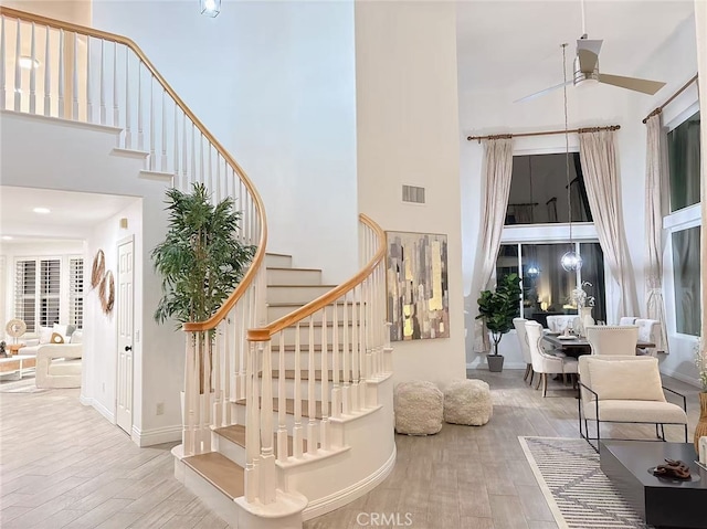 staircase featuring a towering ceiling, ceiling fan, visible vents, and wood finished floors