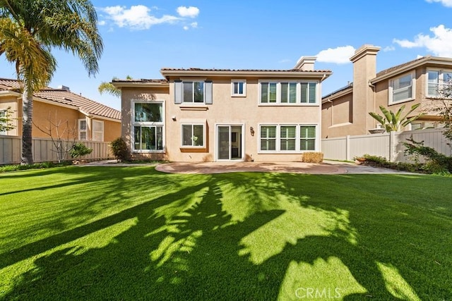 back of house featuring a lawn, a patio, a fenced backyard, a chimney, and stucco siding